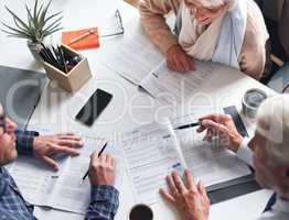 A mature couple meeting with a financial advisor to discuss retirement plans from above. A senior couple meeting a banker to sign contracts together. A mature couple reading and signing documents