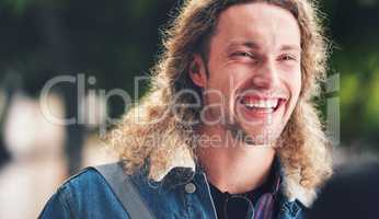 A cheerful handsome man with curly hair in the park. A happy young man laughing relaxing outside in the park. A young handsome man with blonde curly hair spending time in the garden