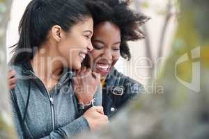 Two cheerful friends hugging one another and laughing during a trip to the park. A happy young woman affectionately hugging her friend. Two friends smiling and hugging outside in the park