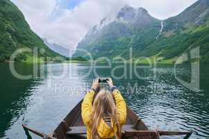 Adventure woman in row boat taking photo on smart phone of beautiful fjord lake for social media