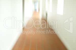 A blurry tiled hallway with white walls and sun shining through the open windows. An empty hospital, clinic or school corridor