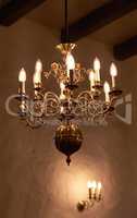 Antique brass chandelier with candle light bulbs hanging from roof or ceiling in a historic,midieval building and vintage room. Shiny ornamental, old fashioned and ancient light fixture in a mansion