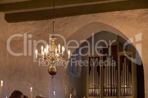 Old fashioned brass chandelier with candle light bulbs hanging from roof or ceiling in a historic building and vintage room. Shiny ornamental, medieval, ancient and antique light fixture in a mansion