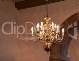 Old fashioned brass chandelier with candle light bulbs hanging from roof or ceiling in a historic building and vintage room. Shiny ornamental, medieval, ancient and antique light fixture in a mansion