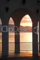 Beautiful sunset over lake through architectural built archways. Silhouette designed archways forming multiple archways overlooking mountains and ocean at dusk. Exploring buildings in travels overseas