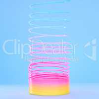 Spiral slinky toy isolated against a blue background. Closeup of a colourful retro plastic toy stretching, twirling and coiling. Spring toy for children to play and fidget with for fun and learning