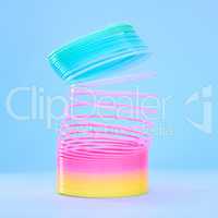 Closeup of a colourful flexible plastic rainbow slinky toy in stretched out motion isolated against a blue background. Entertaining childhood color item for playing, fun and games. Spirals leading in a upward direction