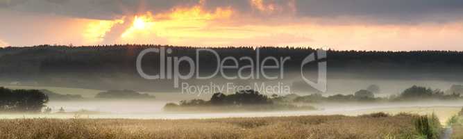 Landscape view of fog over remote field with copy space at sunset. Mist covering a vast expanse of countryside meadow in Germany at dawn. Smoke from wildfire or bush fires rolling over nature reserve