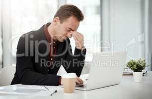 Dealing with the stress of a difficult day. a young businessman looking stressed out while working on a laptop in an office.