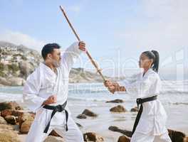 The harder you train, the shorter the fight. Shot of two young martial artists practicing karate with a wooden katana on the beach.