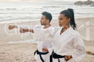 You can only fight the way you practice. Shot of two young martial artists practicing karate on the beach.