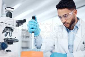 One mixed race male scientists wearing safety goggles and a labcoat while conducting medical research experiments with pipette and test tubes in a lab. Recording his findings for future investigation