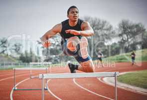 Navigating obstacles with ease. Full length shot of a handsome young male athlete practicing hurdles on an outdoor track.