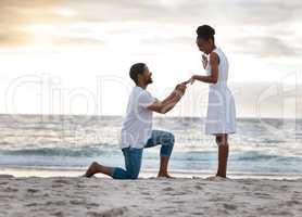 Boyfriend asking his girlfriend to marry him while standing on the beach together. African american man proposing to his girlfriend by the seashore. Young happy couple getting engaged on holiday