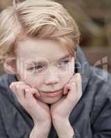 Lonely kid with his hands on his chin thinking. Young little teen kid outside on a playground alone. Cute caucasian male child serious. Bored teenage boy face sitting outdoors in a park alone.