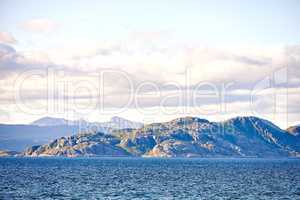 Scenic view of sea, mountains, rocks and boulders in Norway. Tidal ocean water waves, blue sky with clouds and copy space. Travel and tourism overseas and abroad to a remote and peaceful destination