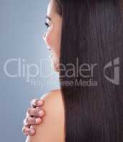 Close up of a young woman with beautiful long smooth hair touching her shoulder. Young mixed race woman with luxurious straight and shiny brown hair. Healthy hair against studio background