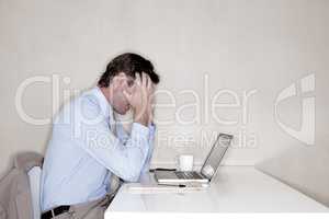 This job is giving me a headache. A businessman sitting at his desk and looking hopeless with his head in his hands.