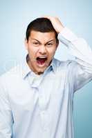 These are the days I hate. Shot of a young man pulling his hair in frustration against a studio background.