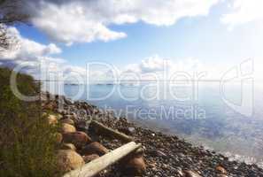 Copyspace at sea with a rocky shore and cloudy sky background. Calm ocean waves at a coast with kayaks cruising in the horizon. Scenic and picturesque landscape view for a peaceful summer holiday