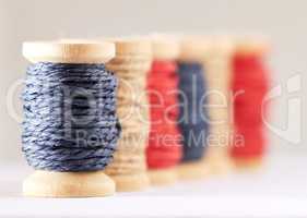 Many rolls of coloured yarn or string lined up in a row in studio isolated against a grey background. For the production of textiles, sewing, crocheting, knitting, weaving, embroidery or rope making