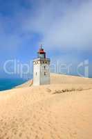 Deserted lighthouse by the sea with blue sky in the background on a sunny day. A lighthouse in between the sandy area surrounded by water and cloudy sky. The mysterious old tower alone in the desert
