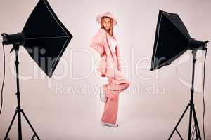 Serious young mixed race woman posing in trendy fashionable clothing while standing in a studio shoot. Confident hispanic woman posing in pink clothes in a studio with bright lights