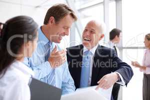 Sharing a moment of corporate humour. Laughing businesspeople going through documents together in an informal meeting.