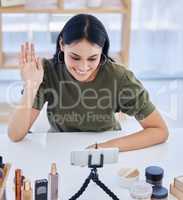 Hispanic beauty blogger waving at her smart phone while recording a video or broadcasting live. Beautiful young influencer sharing her beauty products and regime