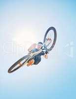 Man showing his cycling skills while out cycling on a bicycle outside. Adrenaline junkie practicing a dirt jump outdoors. Male wearing a helmet doing tricks with a bike. Hovering, passionate and free