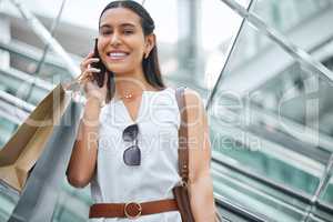 Trendy young woman talking on a cellphone while out on a shopping spree. Female enjoying retail therapy while staying connected with her smartphone. Calling to find a sale and discount. Planning to spend money