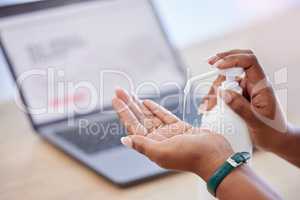 Businessperson holding a bottle and using hand sanitiser while working in an office. Business professional using sanitiser to protect from disease and infection. Person cleaning their hands with sanitiser at work