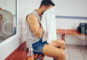 Young player wiping his face with a towel. Tired man cleaning his face with a towel after a squash match. Squatch player sitting in his gym locker room. Mixed race man taking a break after a match