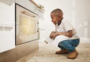 Cant wait to taste these. Shot of a little boy watching his baked goods cook in the oven at home.