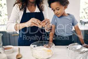 Closeup of female hands cracking a egg into a bowl while baking at home with her son. Woman adding ingredients to a glass bowl on the counter at home while baking with her child