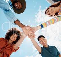 Low angle view of diverse group of people standing huddled together with hands piled in the middle. African American woman with an afro. Millennial social clique stacking hands in unity and support