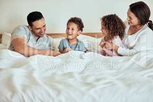 Mixed race family lying in bed, smiling and playing. Latino parents having fun with their little cute kids. Brother and sister in bed with their mother and father at home in the morning