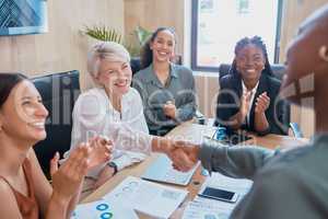 Handshake between business women. Two diverse colleagues shaking hands during a meeting in the boardroom. Congratulating her on a job well done while coworkers clap in acknowledgement of achievement