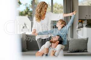 Happy caucasian family bonding at home. Excited little boy sitting on his fathers shoulders and holding his mothers hands while pretending to fly for play and fun. Loving parents relaxing with son