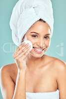 Wiping my way to clear skin. Shot of a young woman applying product to her face using a cotton pad against a studio background.