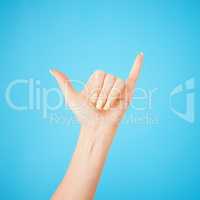 Hey, whats up. Studio shot of an unrecognisable woman showing a shaka hand sign against a blue background.
