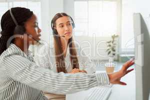 Young hispanic call centre telemarketing agent discussing plans with a colleague while working together on a computer in an office. Consultants troubleshooting solution for customer service and sales support