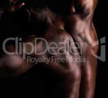 Closeup rearview shot of the back of a black african american man posing in studio isolated against a black background. The human body in masculine and muscular form. A show of strength and dedication