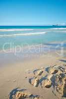 Waves washing onto sandy beach shore with footprints on a tropical and exotic resort with clear blue sky background and copyspace. Relaxing summer seascape to enjoy a peaceful holiday