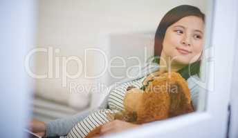 Shes already bought babys first teddy. an attractive young woman relaxing with a teddy bear on the sofa at home.