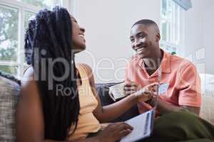 Happy young african american couple talking and bonding while sitting at home. Handsome man drinking coffee while girlfriend shops online. Smiling woman holding credit card and laptop to do payment