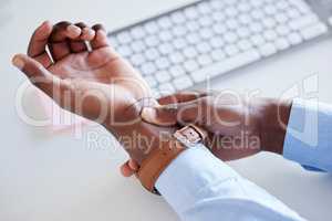 Closeup of one african american businessman from above suffering with aching wrist pain while working on a computer in an office. Black guy hurt with carpal tunnel syndrome disability. Feeling discomfort cramp in arm and hand