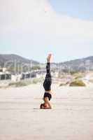 It takes patience to master this pose. a young woman doing a headstand while practising yoga at the beach.