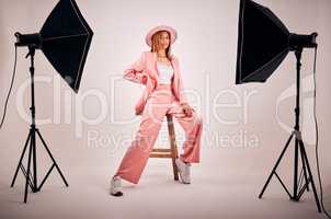 Portrait of a young mixed race female posing in trendy fashionable clothing while chilling on a chair in a studio shoot. Hispanic woman showing the latest fashion collection with a cool style and hat