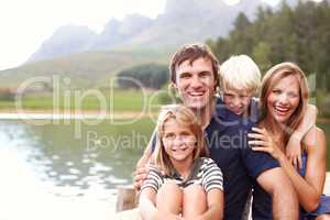 Enjoying the perfect family vacation. Smiling and happy young family sitting on a jetty together.